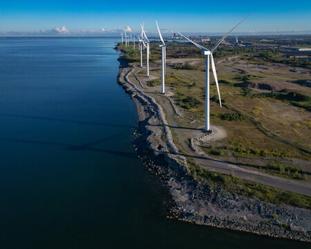 Wind turbines line the coast of a large lake on a sunny day