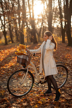 Young woman with bicycle enjoys autumn park with fallen leaves and