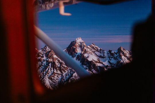 Snow covered mountain peaks framed by interior of a small aircraft.