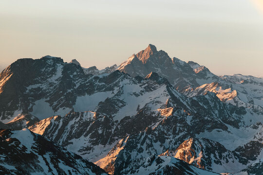 Snow covered mountain ridges catch warm sunrise light.