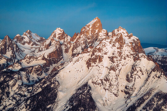 Jagged snow covered mountain peaks glowing in soft morning light.