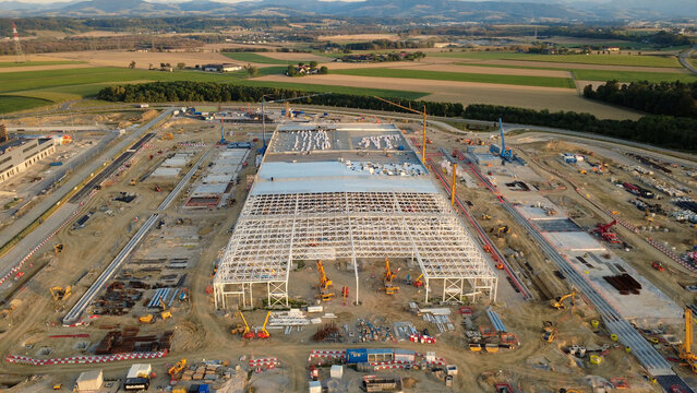 Aerial view of a large data center construction site featuring a steel frame structure, multiple cranes, and heavy machinery in the rural landscape of Kronstorf, Upper Austria, Austria.