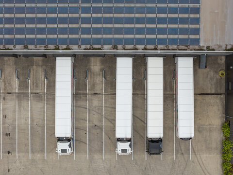 Aerial view of semi-trucks parked at a logistics distribution center with solar panels on the warehouse roof in Genk, Flanders, Belgium.