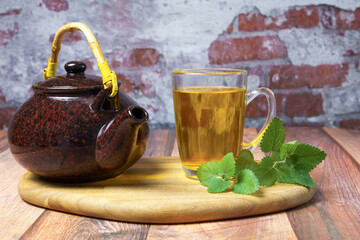 Ceramic teapot and glass mug filled with warm herbal tea lemon balm , accompanied by fresh mint leaves on a wooden board © JOSEANTONA