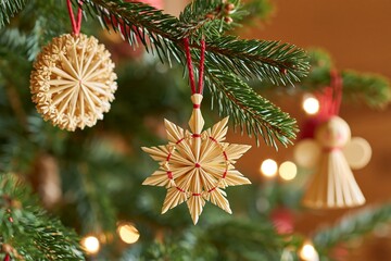 Obraz premium Traditional straw star, round straw ornament and wooden angel hanging from evergreen branches with red cords and warm lights, detailed Christmas tree decorations