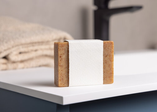 Brown soap bar with blank label mockup near beige towel in blue bathroom closeup