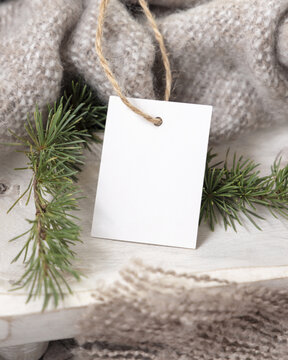 Vertical gift tag mockup near beige knitted blanket and fir branches. Rustic Christmas packaging