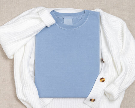 Light blue folded t-shirt mockup near knitted cardigan and palm leaf, template for print on demand