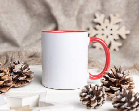 Blank white and red coffee mug mockup near wooden Christmas decor, pine cones and beige blanket