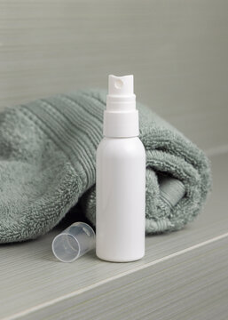 White cosmetic spray borttle mockup on sage green towel in bathroom, unbranded packaging