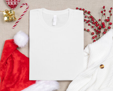 White t-shirt mockup near red Christmas decor, top view with copy space. Holiday template