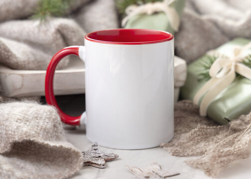 Blank white coffee mug mockup near wooden Christmas decor, pine cones and beige blanket closeup