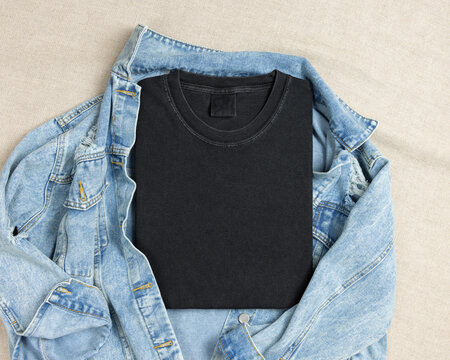 Blank washed black folded shirt mockup over blue denim jacket, crewneck template for print on demand