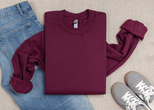Dark red unisex sweatshirt mockup, folded flat lay with denim shorts and grey sneakers, top view