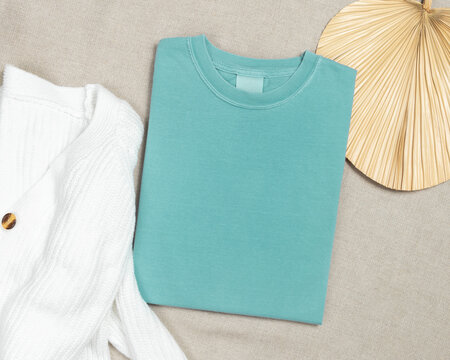 Washed light green folded t-shirt mockup near knitted cardigan and palm leaf, template for print on demand