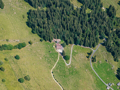 Aerial view of a mountain chalet nestled in the green pastures of Justistal near Niederhorn, with winding roads and dense pine forests in the Bernese Alps, Sigriswil, Bern, Switzerland.