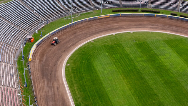 Aerial view of a tractor grooming the dirt track at the speedway stadium with empty seating and a green infield in Gdansk, Poland.