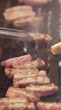 Chef turns cevapi with tongs on grill at restaurant, grilling traditional balkan sausage during outdoor summer barbecue, cooking dinner for guests