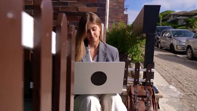 Professional young caucasian woman sitting on the steps outside a building, focused on typing and working on her laptop computer, embracing a modern and flexible work style