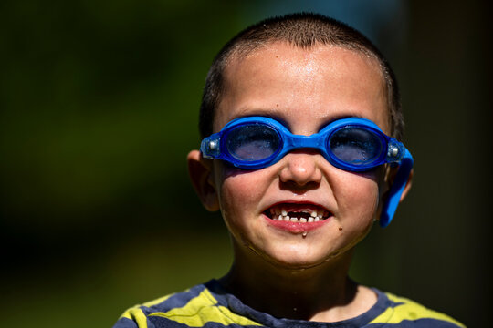 Portrait of a young smiling boy wearing blue swimming goggles on a sunny day.