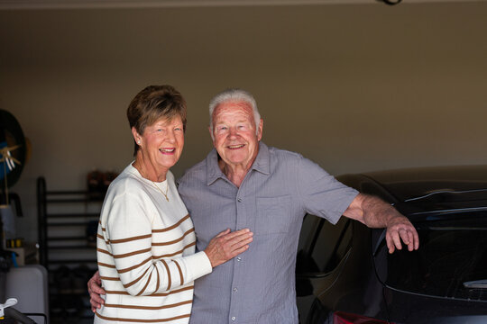 portrait of happy seventysomething senior couple together in their garage beside car