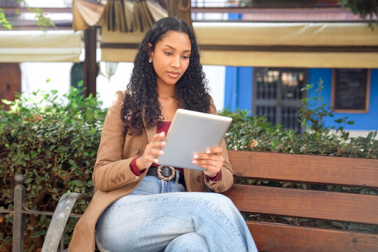 Female individual engrossed in reading digital content amidst lush trees and sunlight