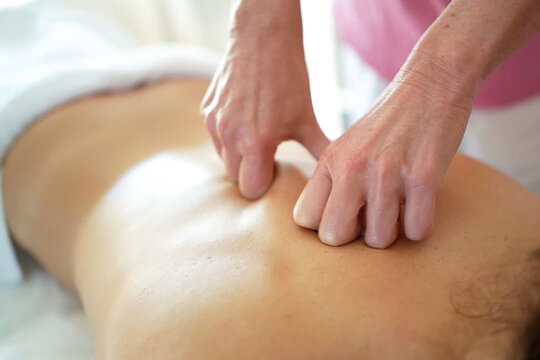 massage session with hands massaging back in relaxed environment, oil or lotion on skin, pink shirt, tan skin, white background, close-up focusing on hands and back.