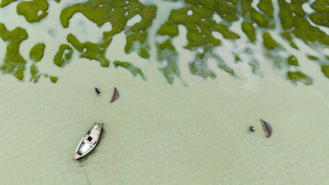 Aerial view of fishermen using traditional nets in shallow waters with a wooden boat in Patharghata, Barisal Division, Bangladesh.