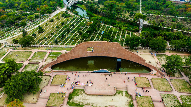 Aerial view of Rayer Bazaar Memorial with its iconic curved brick wall, reflecting pool, and black monolith surrounded by lush parkland in Dhaka, Dhaka Division, Bangladesh.