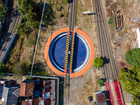 Aerial view of a railway turntable with yellow and black hazard markings surrounded by tracks and vegetation in Cilacap, Central Java, Indonesia.