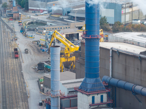 Aerial view of industrial infrastructure at Genk-Zuid Rechteroever featuring a blue chimney, yellow crane, and railway tracks at the steel manufacturing facility in Genk, Vlaanderen, Belgium.