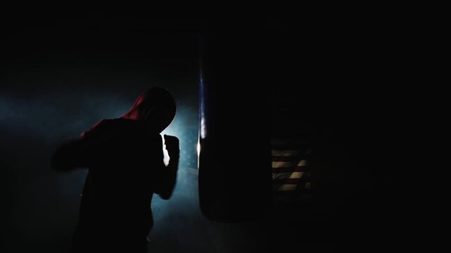 Boxer training with punching bag in dark studio with atmospheric smoke and american flag backdrop.