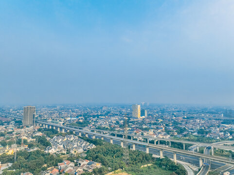 Aerial view of Cikunir area featuring a prominent elevated highway and railway overpass winding through dense urban housing and lush greenery in Kecamatan Bekasi Selatan, Jawa Barat, Indonesia.