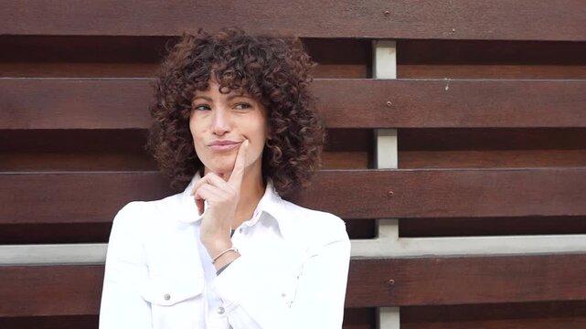 A Stylish Woman with Beautiful Curly Hair Posing Elegantly Against a Modern Urban Background