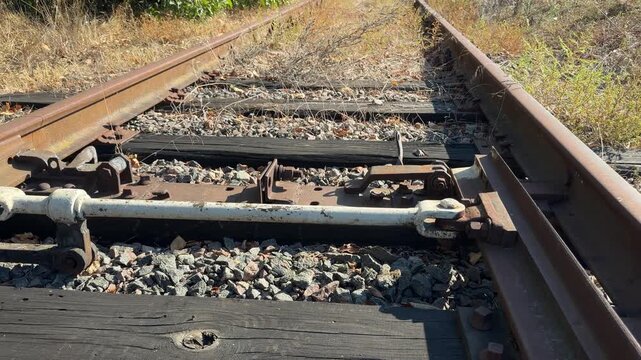 Low angle view moving over a rusty railroad switch to a long perspective of an overgrown, disused track under a blue summer sky