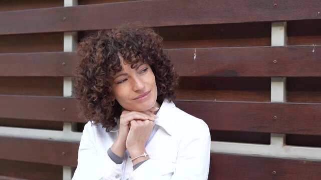 A Contemplative Young Woman with Beautiful Curly Hair Posing Against a Wooden Background