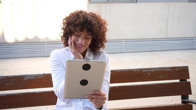 A woman happily enjoying engaging digital content on her tablet while in an urban park