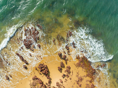 Aerial view of Phillip Island coastline featuring rugged rocks on a golden sandy beach with turquoise ocean waves crashing against the shore in Bass Coast Shire, Victoria, Australia.