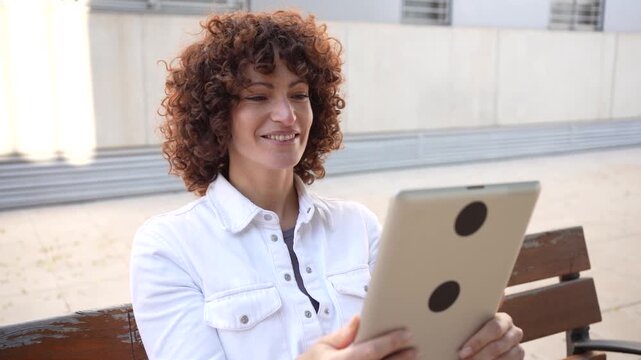A young woman deeply engaged with her tablet while sitting in a pleasant outdoor setting