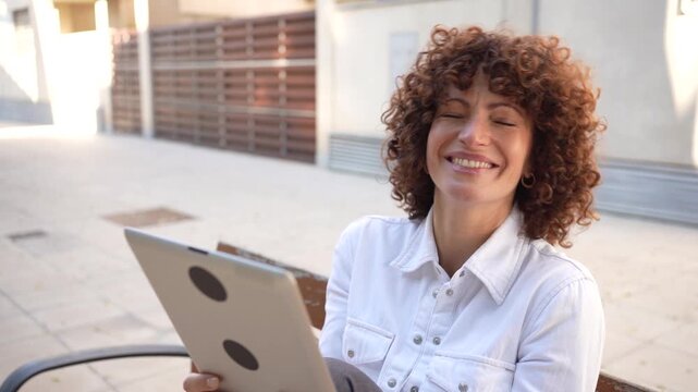 A thoughtful woman sits outdoors, engaged with her tablet, enjoying leisure and contemplation