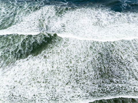 Aerial view of Depok Beach with powerful ocean waves breaking and white sea foam patterns on the water surface, Special Region of Yogyakarta, Indonesia.