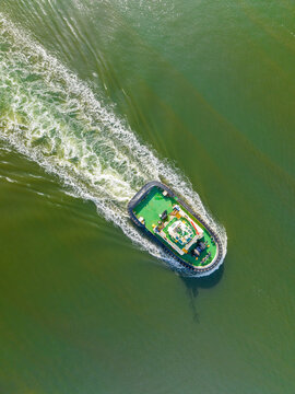 Aerial view of a tugboat moving through green water leaving a white wake in Williamstown, Victoria, Australia.