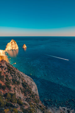 Serene blue cove crystal clear water rugged limestone cliffs rocky Greek coast summer bay vertical view. Peaceful nature seascape landscape scene. Scenic Mediterranean travel tranquil wellbeing escape