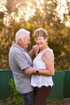 portrait of woman in her seventies smiling while dancing with her husband backlit by golden light
