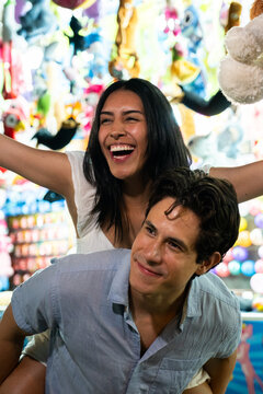 Smiling young couple having fun on a piggyback ride at the fair