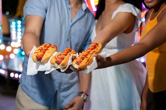 People enjoying hot dogs with ketchup and mustard at a vibrant outdoor fair