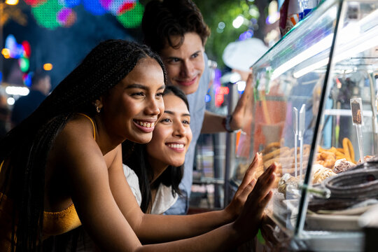 Diverse friends smiling while choosing food from a illuminated display at a night fair