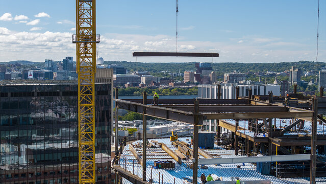 Aerial view of Kendall Square construction site with steel beams, a yellow crane, and workers on the building frame in Cambridge, Massachusetts, United States.