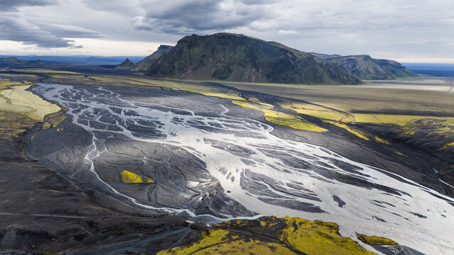 Aerial view of the braided river system at Thakgil, featuring dark volcanic sand, vibrant green moss, and rugged mountains under a cloudy sky in Vik, Myrdalshreppur, Iceland.