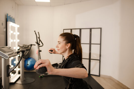 Fit woman in EMS suit doing arm flyes exercise with spiky massage balls indoors